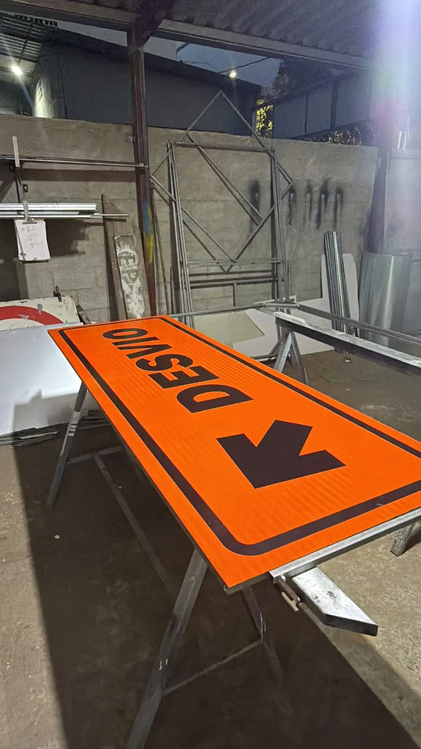Placa viária laranja de desvio recém-produzida sobre cavalete na oficina