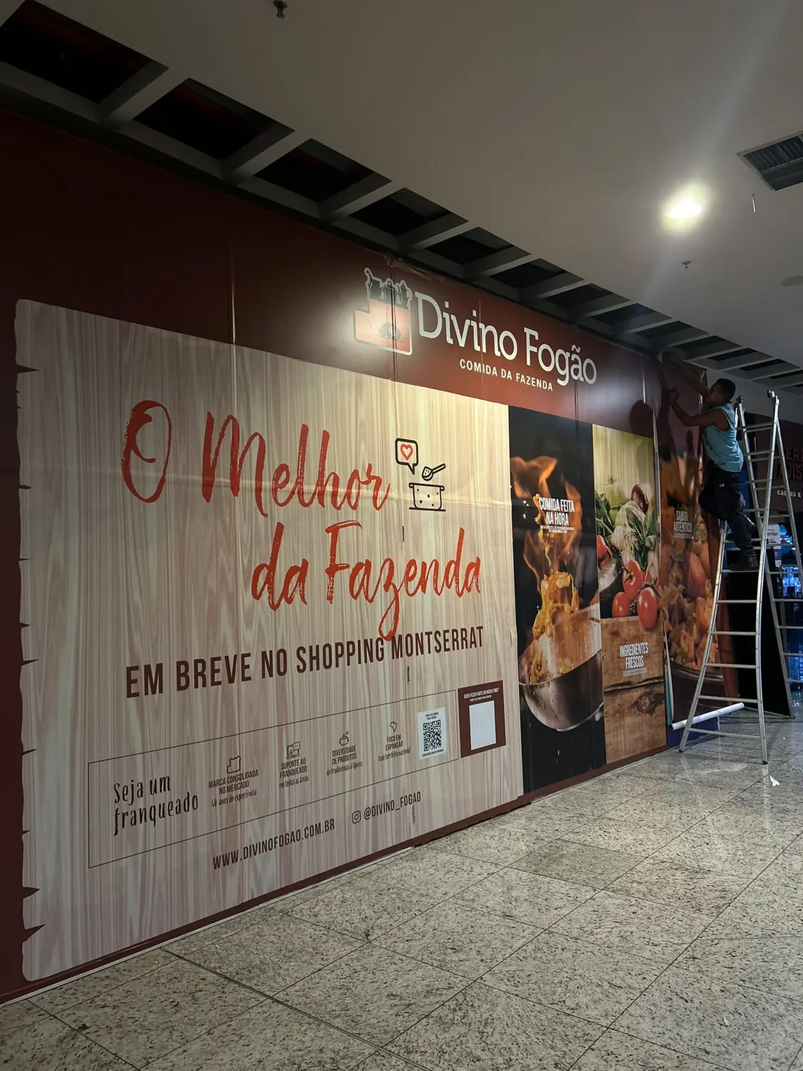 Tapume de loja em shopping com a marca Divino Fogão, instalado com escada