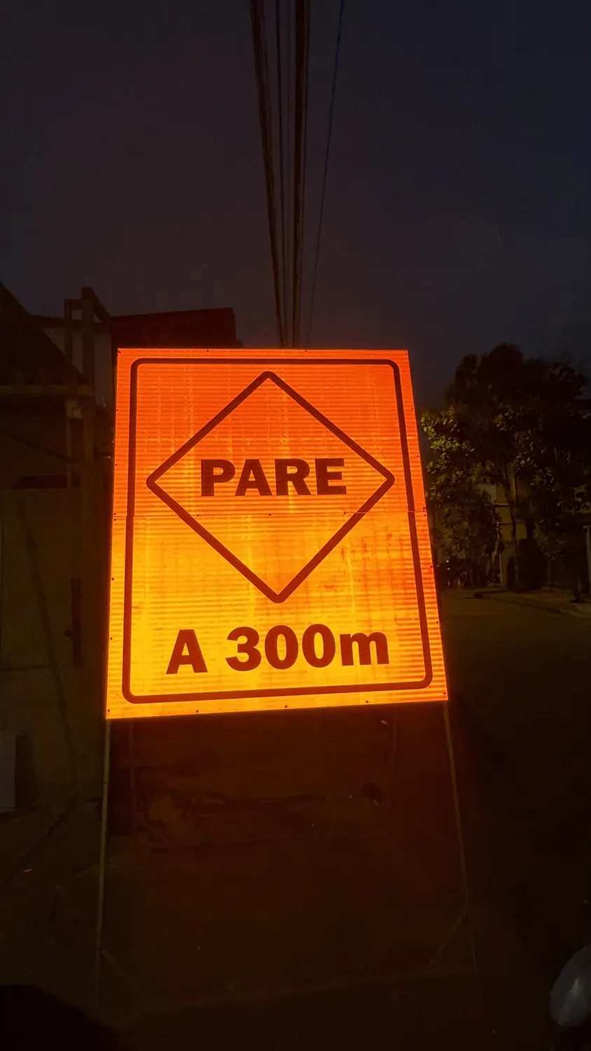 Placa viária de PARE a 300 metros refletindo luz à noite