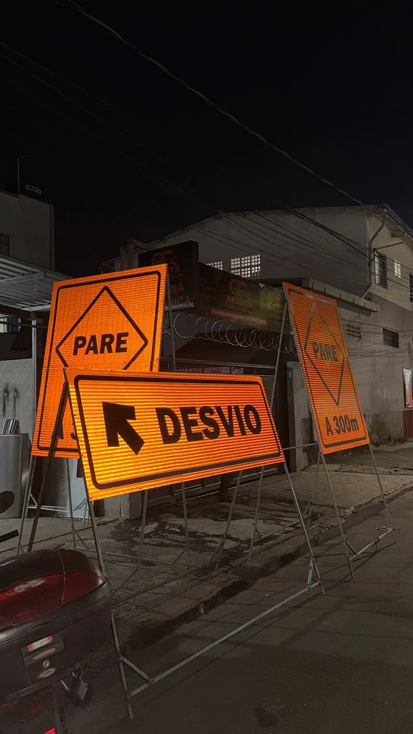 Conjunto de placas viárias de PARE e desvio em material refletivo, montadas na rua à noite
