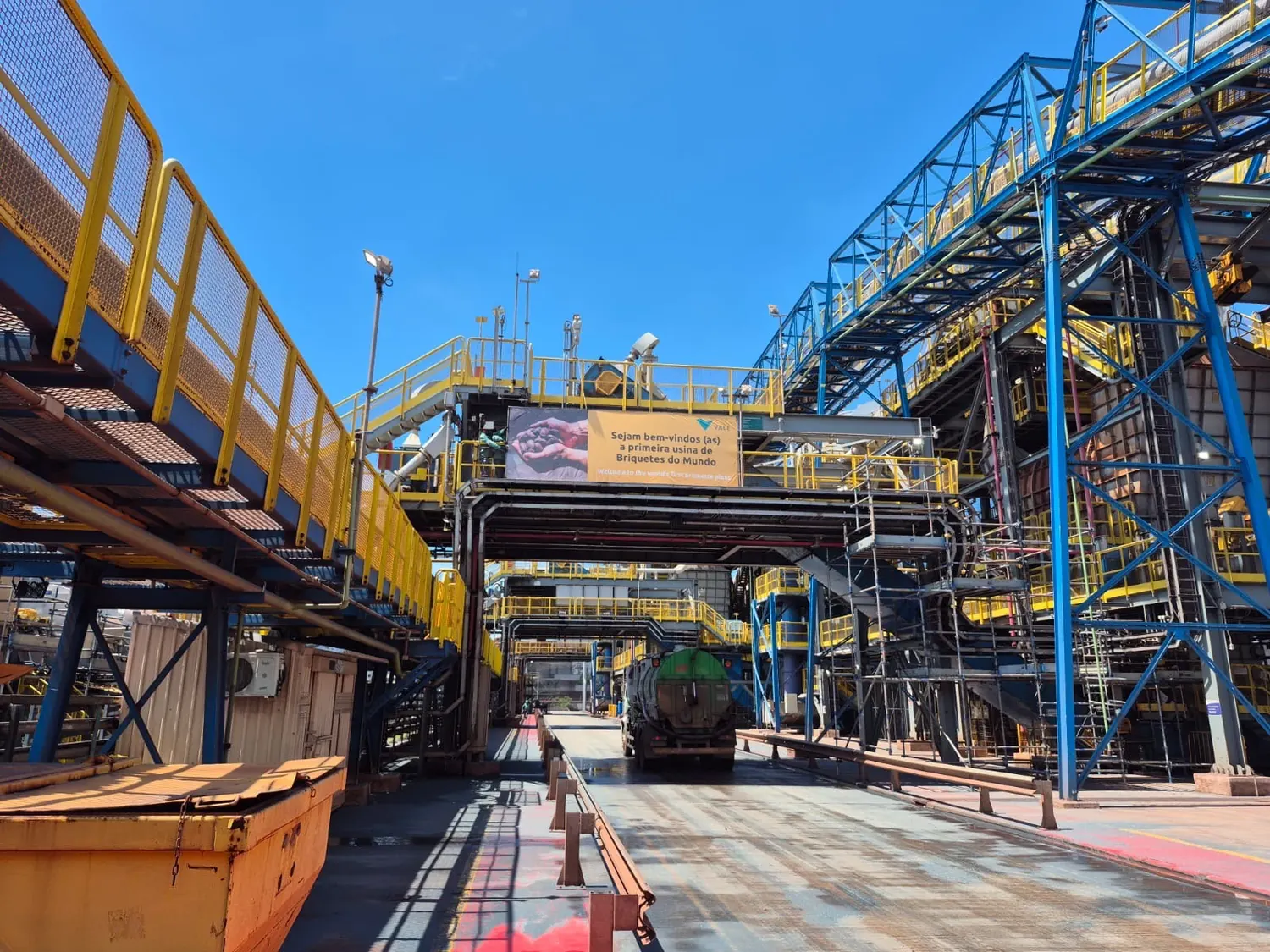 Faixa suspensa de boas-vindas instalada entre passarelas de uma usina industrial
