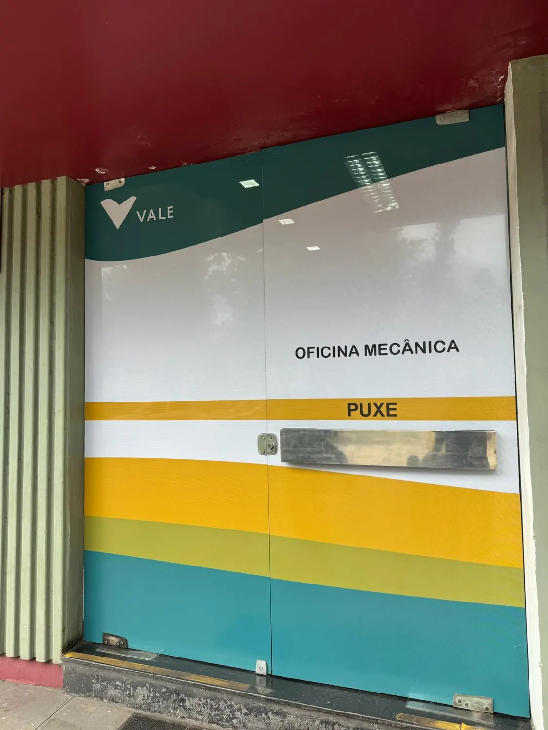 Porta de vidro dupla adesivada com faixas verdes e amarelas e a identificação Oficina Mecânica