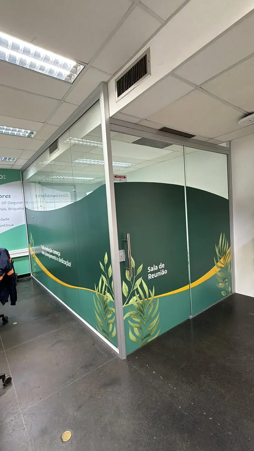 Divisória de vidro adesivada em verde com folhagem e a identificação Sala de Reunião